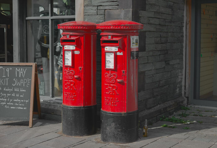 Two classic red Royal Mail postboxes standing side by side outdoors, sparking mind-boggling conversations about adults.