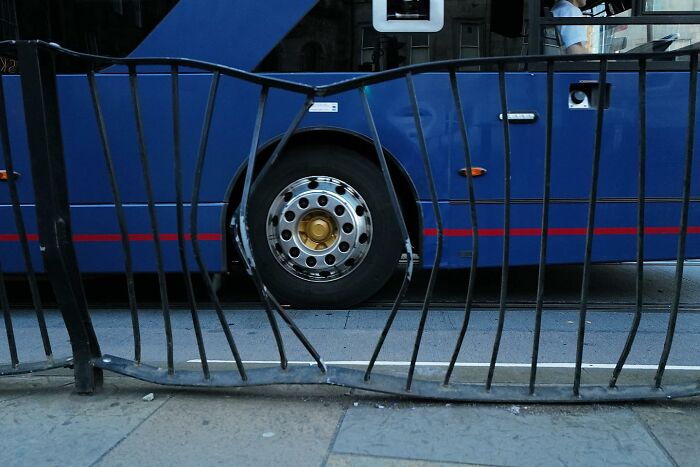 Bent metal fence in front of a blue bus tire, a street photo capturing the funny side of urban life.