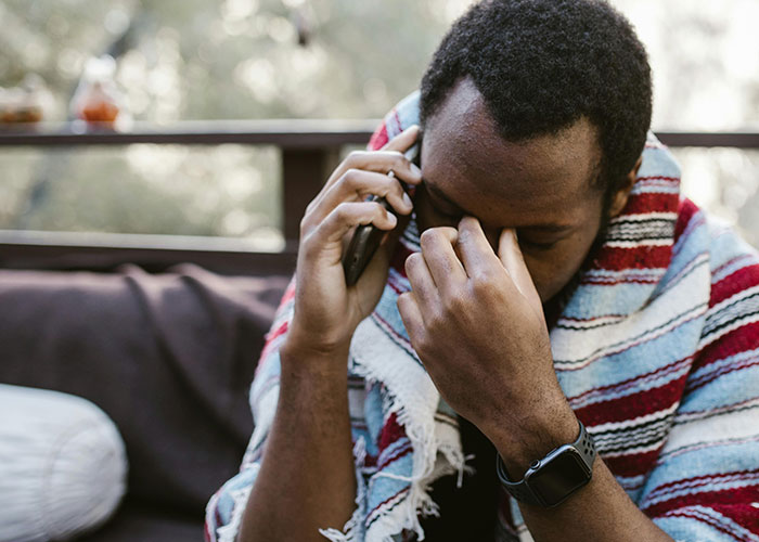 Man wrapped in a blanket showing stress and worry while talking on the phone, linked to anaphylactic shock and food issues.