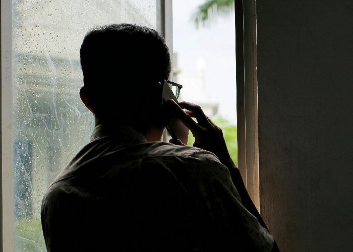 Silhouette of a man making a phone call by a window with rain droplets, conveying a mother poisoned me theme.