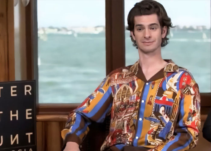 Andrew Garfield sitting by a window wearing a vibrant patterned shirt, showing a united front after interview snub.
