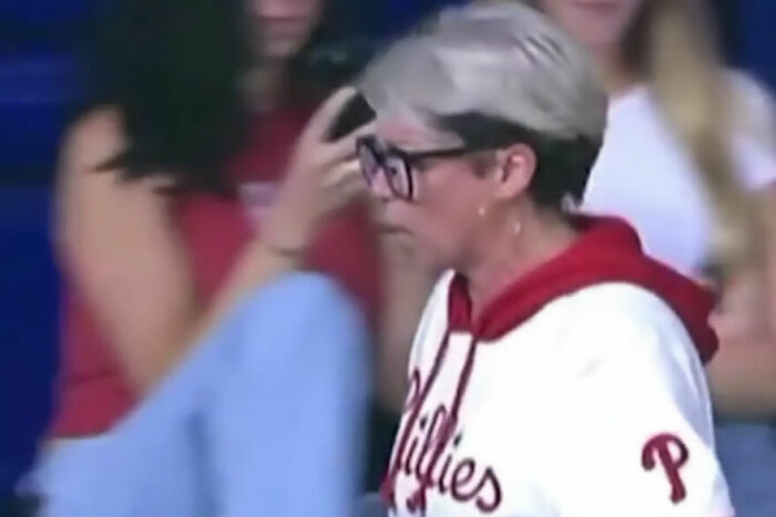 Older woman with glasses in Phillies hoodie at crowded baseball game linked to Karen snatching home run ball incident.