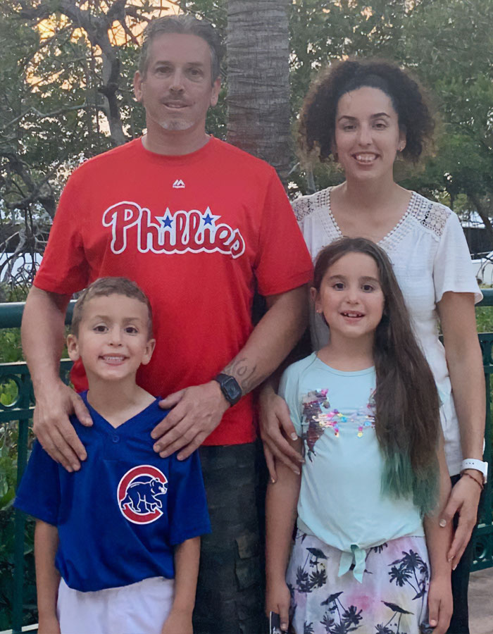 Family of four outdoors, with boy in Cubs shirt and man wearing Phillies shirt, related to company offering 5K to Karen who snatched ball