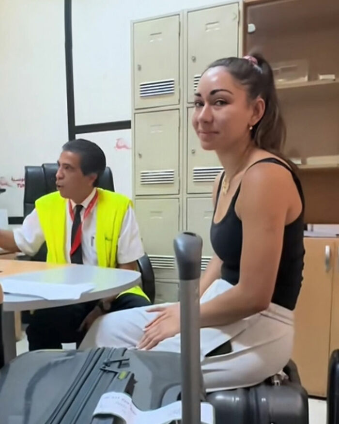 Young confused tourists sitting with luggage at airport, speaking with staff after mistakenly boarding flight to Africa.