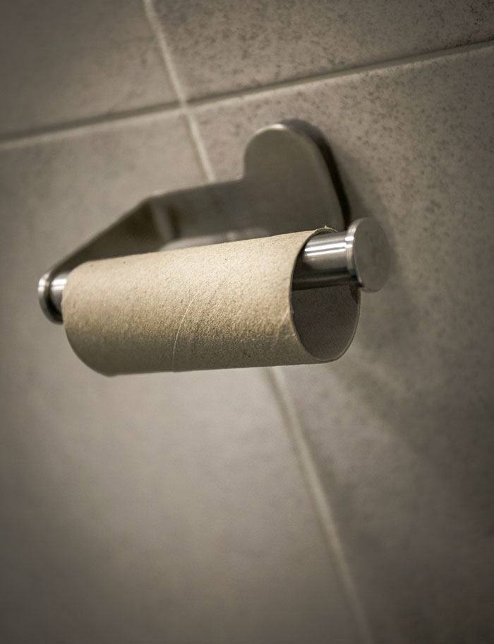 Empty toilet paper roll on a holder against a tiled bathroom wall, illustrating unexpected things men didn’t know about women.