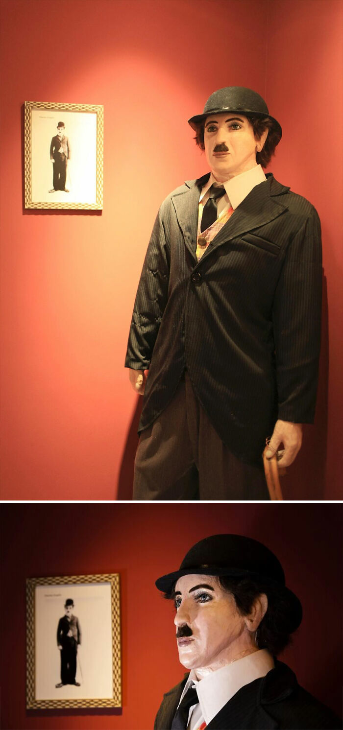 Wax sculpture of a famous figure wearing a suit and bowler hat, displayed against a red wall with framed photo.