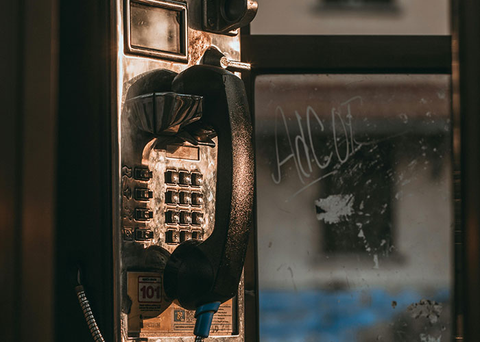 Old public payphone with a black handset hanging, dimly lit, evoking eerie vibes for terrifying true stories.