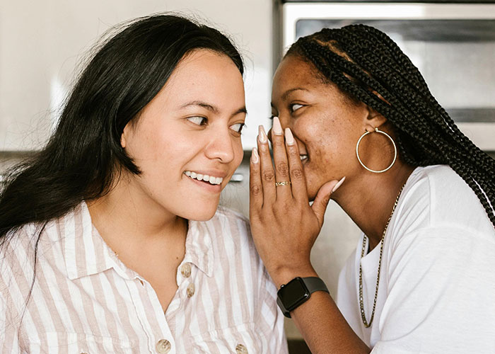 Two women whispering closely, one smiling, illustrating social interaction related to creepy things women do that cross the line.