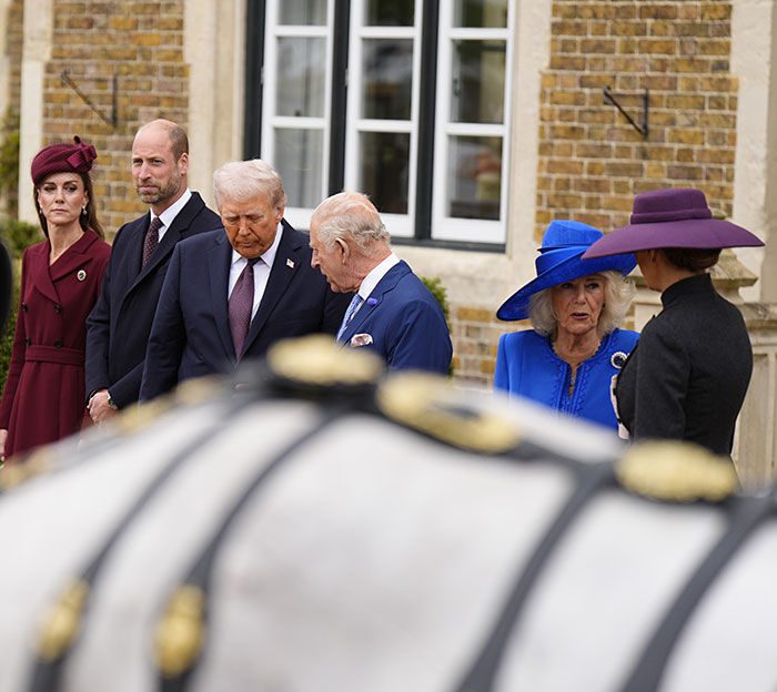 Queen Camilla in blue outfit making an embarrassing gesture to Kate Middleton during Trump visit outdoors.