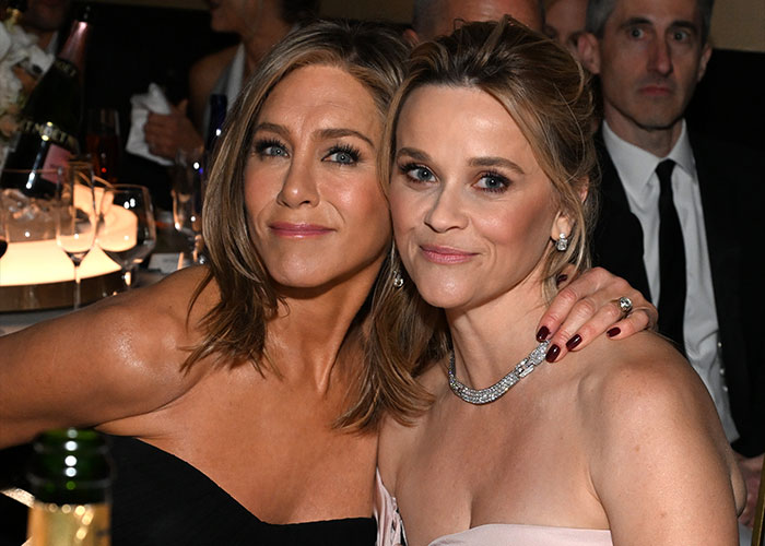Jennifer Aniston and Reese Witherspoon smiling and posing together at a formal event, showcasing their friendship.