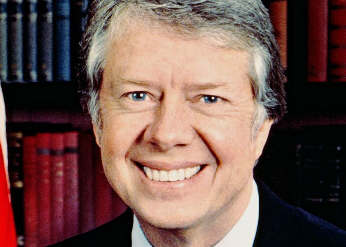 Portrait of a smiling man with gray hair in front of bookshelves, related to historical events causing societal damage.