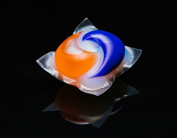 Laundry detergent pod with orange and blue swirls on a black surface symbolizing collapse of common sense.