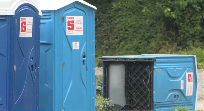 Blue porta-potty units at an outdoor site, one tipped over, related to cop opening fire on teens over prank incident.