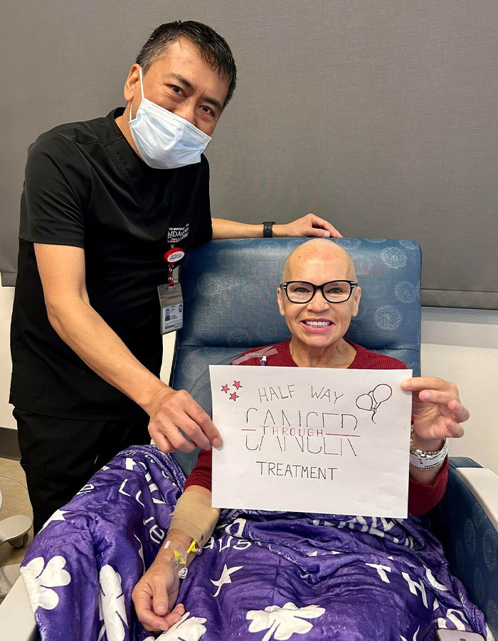 Woman smiling in hospital chair with doctor, holding sign about cancer treatment, highlighting misunderstood symptoms before diagnosis