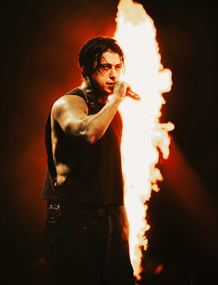 Ex-con rock star performing intensely on stage with flames in the background during a live concert.