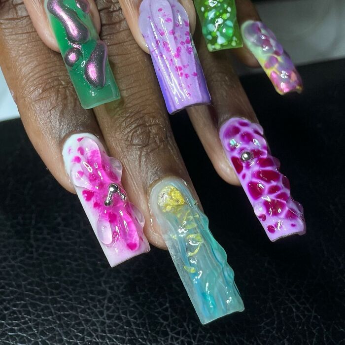 Close-up of hand showing unique 3D textured nail designs in vibrant green, purple, pink, and blue shades.