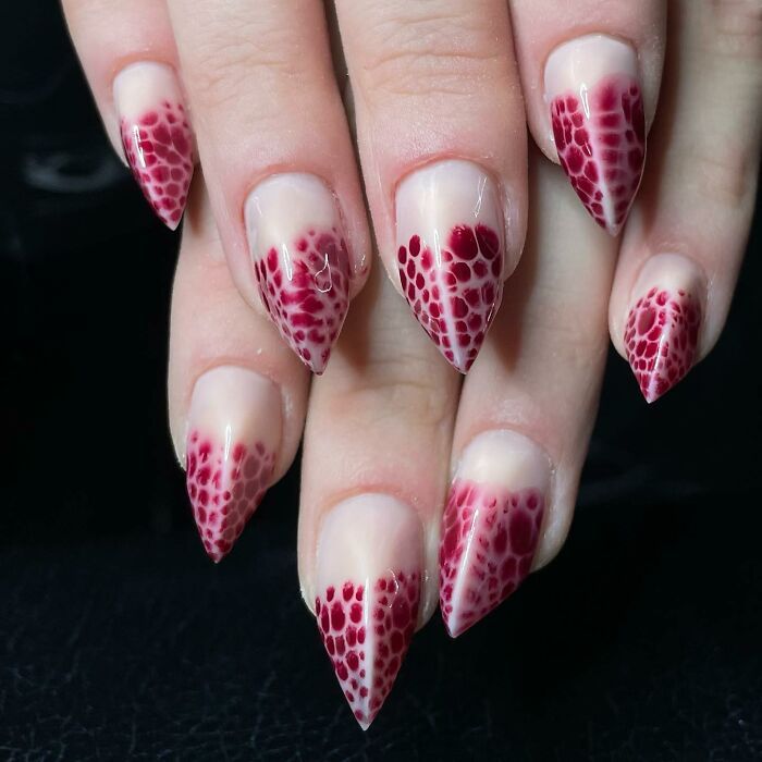 Long, pointed nail designs with red mesh-like patterns on a natural base, showcasing bold and unique nail art styles.