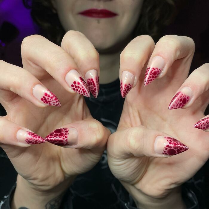 Long, pointed nail designs with red mesh-like patterns on a natural base, showcasing bold and unique nail art styles.