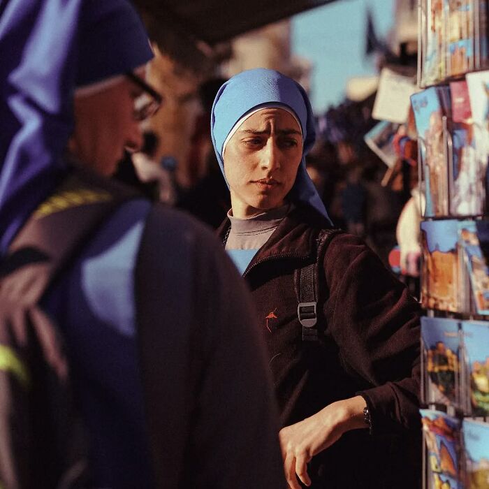 Two women wearing blue headscarves browsing postcards in an outdoor market, captured in a stunning street photo.