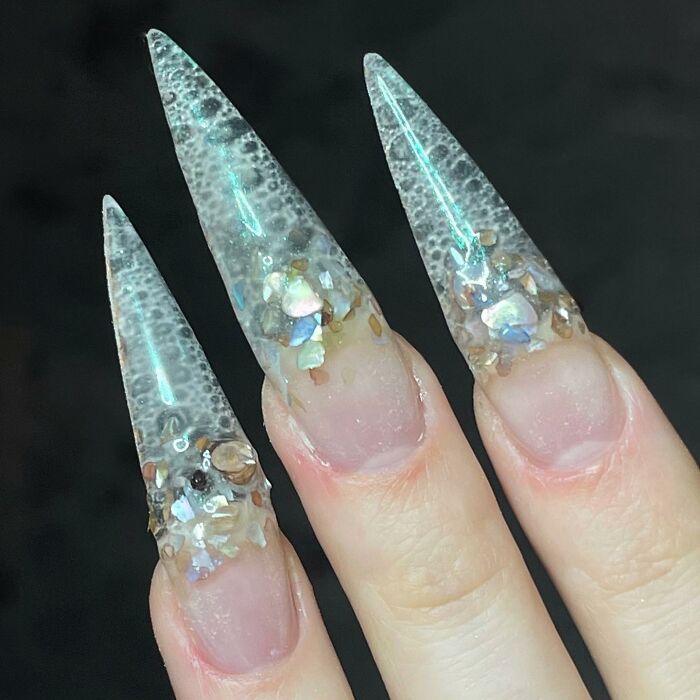 Clear stiletto nail designs with iridescent embellishments and textured details showcasing bold nail design creativity.