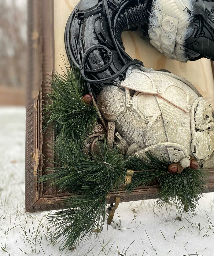Sculpture of a swan made from recycled trash materials displayed in a wooden frame outdoors in the snow.