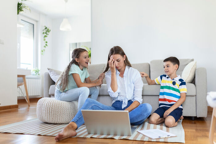 A stressed mother sitting on the floor with laptop, comforted by two children in a bright living room, reflecting life-changing sentences.
