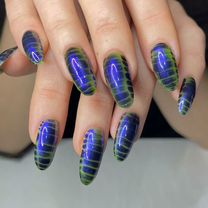 Close-up of hands showing unique blue and green nail designs with a glossy finish, showcasing creative nail art styles.