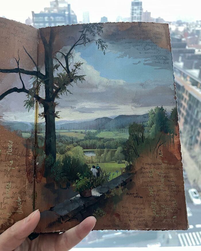 Hand holding a detailed painting by Dina Brodsky depicting a natural landscape with trees and distant hills.