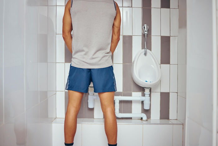 Man standing at a urinal in a public restroom, illustrating unusual dealbreakers in relationships revealed by women.