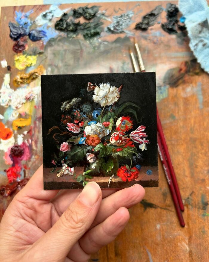 Hand holding a detailed painting of a colorful floral arrangement, showcasing natural world beauty.