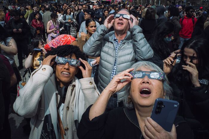 Crowd of diverse people wearing eclipse glasses and looking up during a dramatic striking street photo moment.