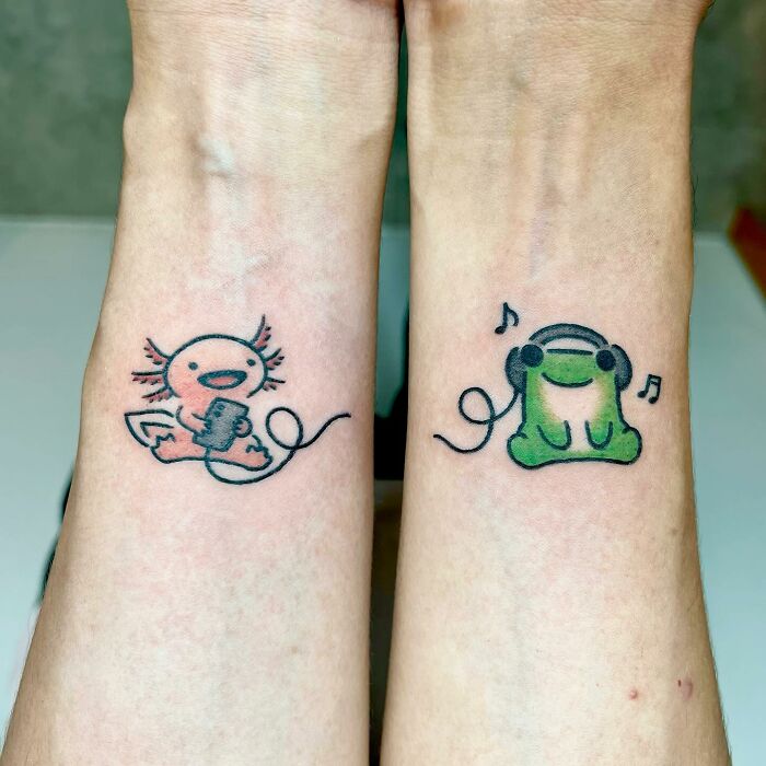Cute frog and axolotl animal tattoos on wrists by Korean artist Buoy, featuring playful and colorful designs with music elements.
