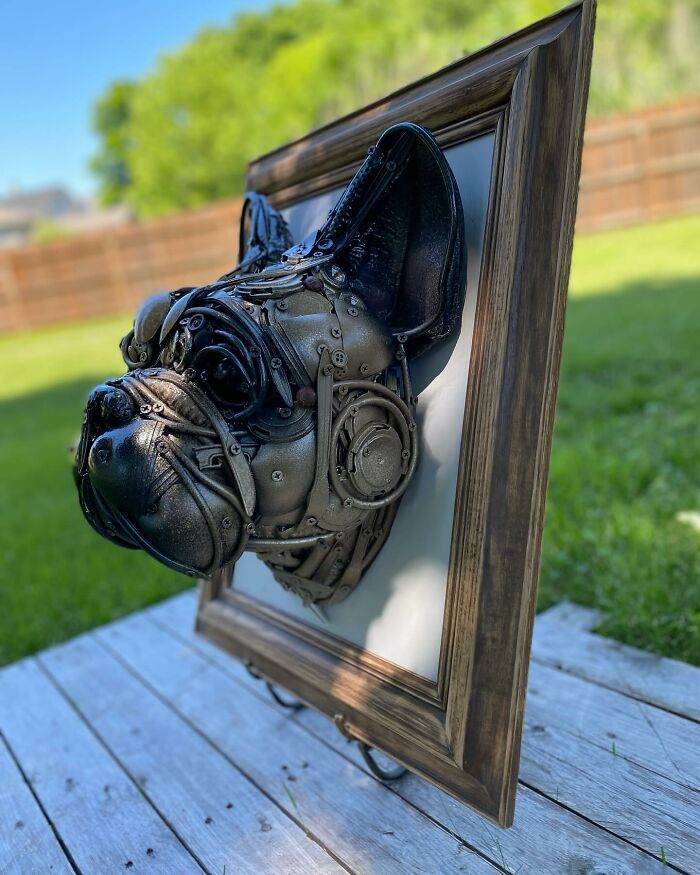 Dog head sculpture made from recycled metal parts displayed in a wooden frame, showcasing trash turned into stunning animal art.