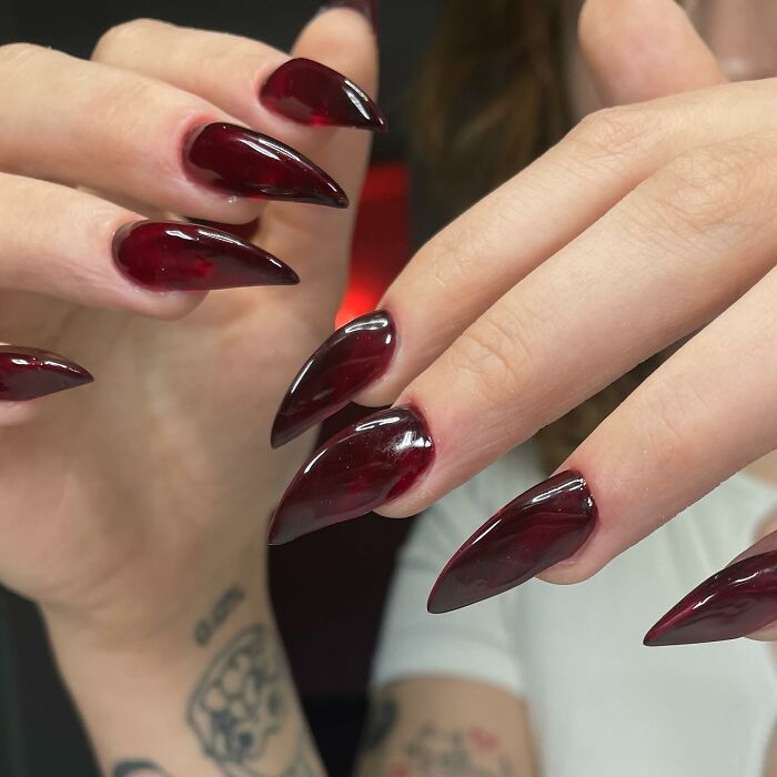 Glossy dark red stiletto nails with a unique swirl pattern, showcasing creative and bold nail designs that break all the rules.