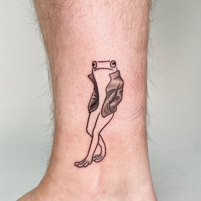 Minimalist adorable frog tattoo with human-like posture wearing a jacket, designed by Korean artist Buoy on ankle skin.