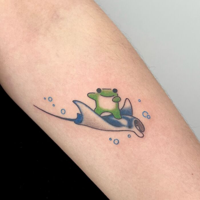 Small adorable frog tattoo riding a blue stingray with bubbles, animal tattoo by Korean artist Buoy on forearm.