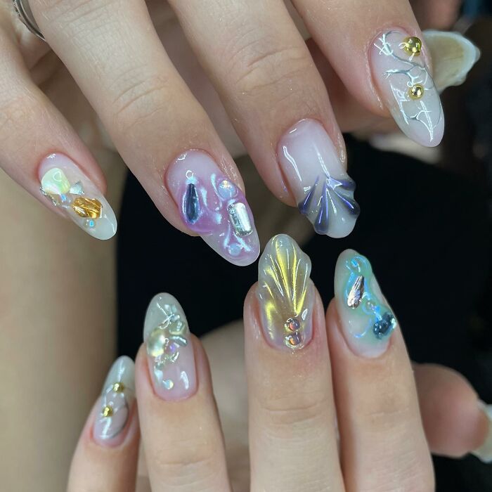Unique nail designs featuring 3D embellishments and iridescent shells on a glossy, translucent base for stunning nail art.