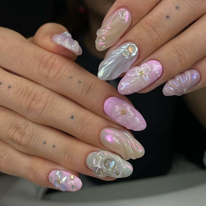 Close-up of unique pink and pearlescent 3D nail designs featuring floral and abstract decorations on manicured nails.