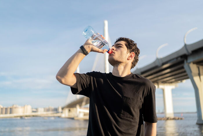 Young man drinking water outdoors near a bridge, illustrating themes of absurd dealbreakers in relationships from women's perspectives.