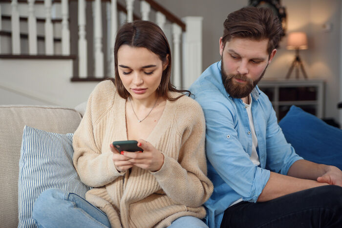 Couple sitting on couch while woman surfs online and man looks over, revealing spouses secret stories discovered unexpectedly.