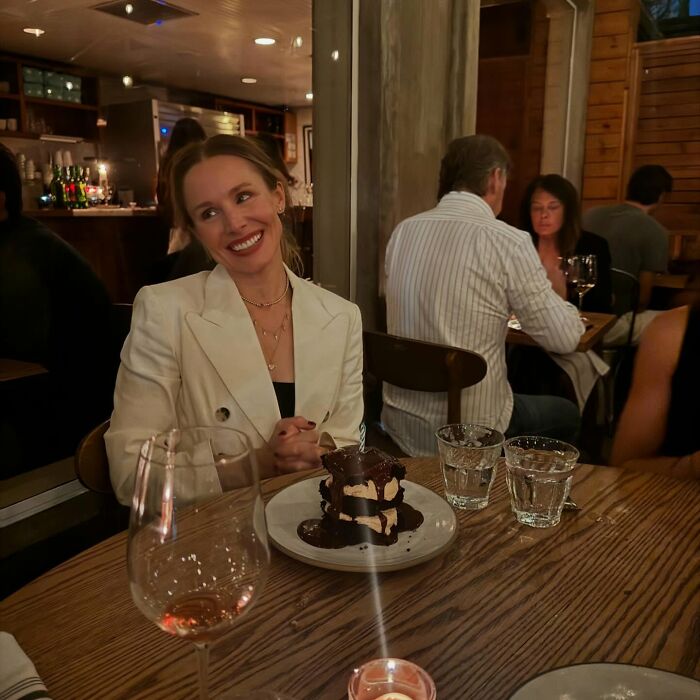 Kristen Bell smiling at a restaurant table with dessert and drinks, showcasing a simple biohacking trick for fitness.
