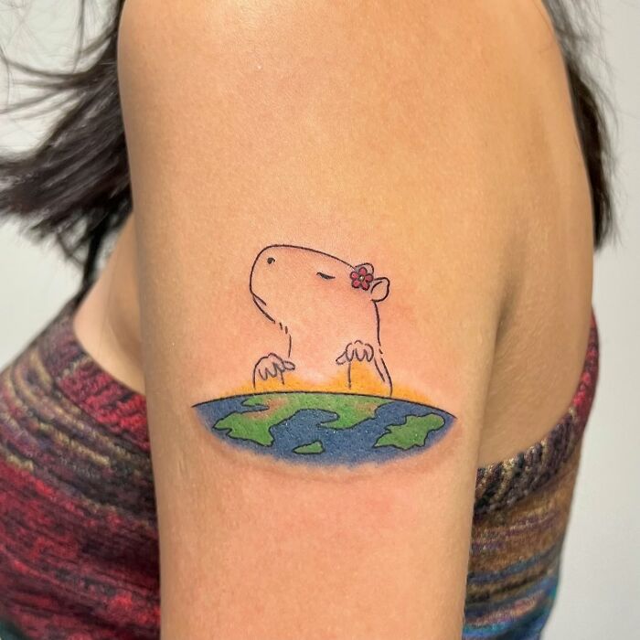 Capybara tattoo with a flower on its head above a colorful earth design, adorable frog and animal tattoos by Korean artist Buoy.