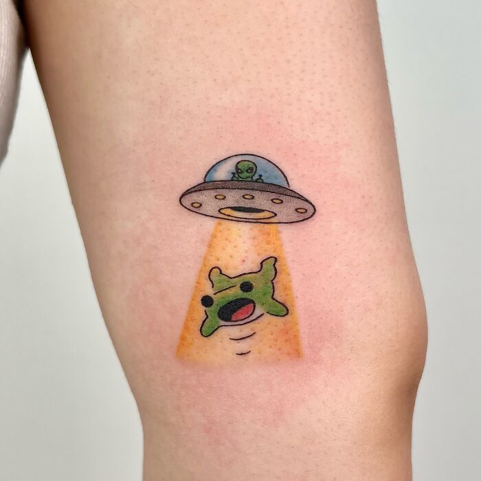 Small adorable frog tattoo being abducted by a UFO with a green alien, colorful animal tattoo by Korean artist Buoy.