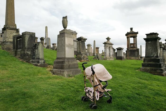 Empty baby stroller left on grass among historic gravestones in a cemetery, a brilliant street photo capturing the funny side.