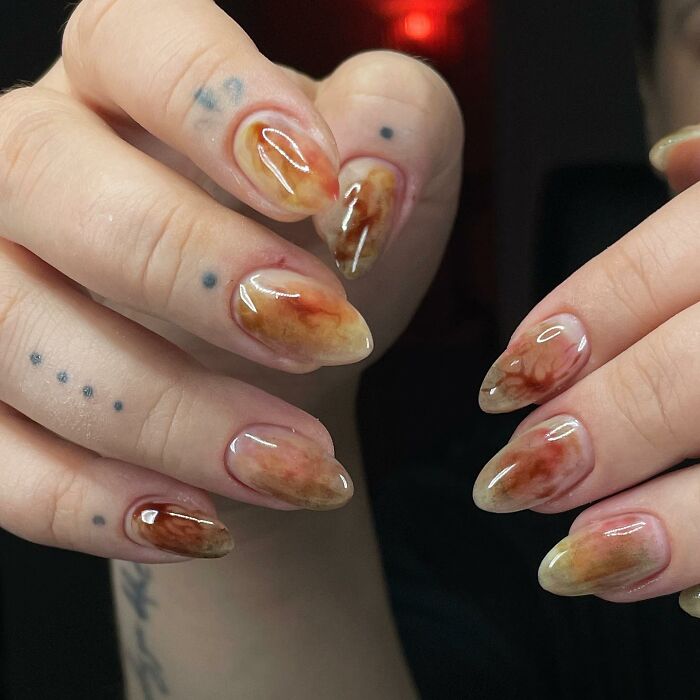 Glossy abstract nail designs with earthy tones on almond-shaped nails, showcasing unique and rule-breaking nail art creativity.