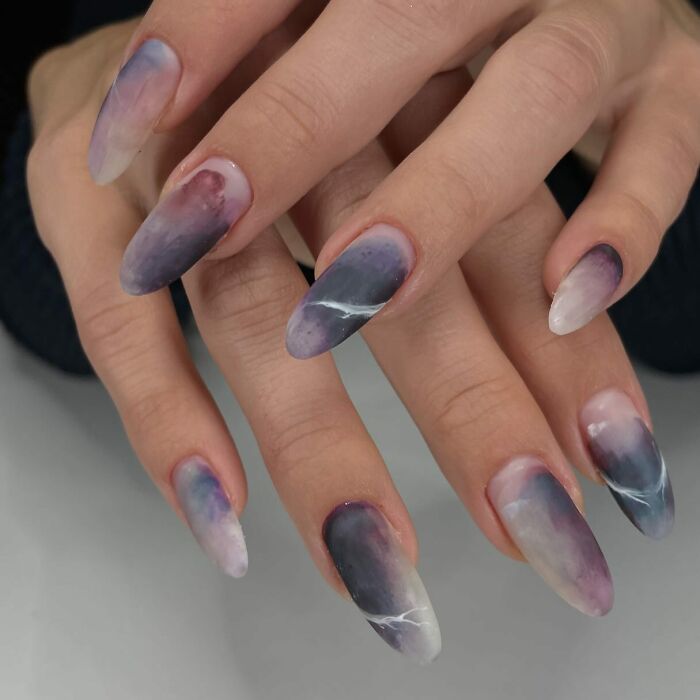 Hand with long nails featuring unique purple and white marble nail designs breaking all the rules with a stunning look.