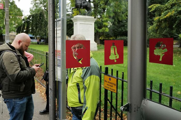 Man in a bright jacket humorously aligned with red street art at a bus stop, capturing the funny side of street photos.