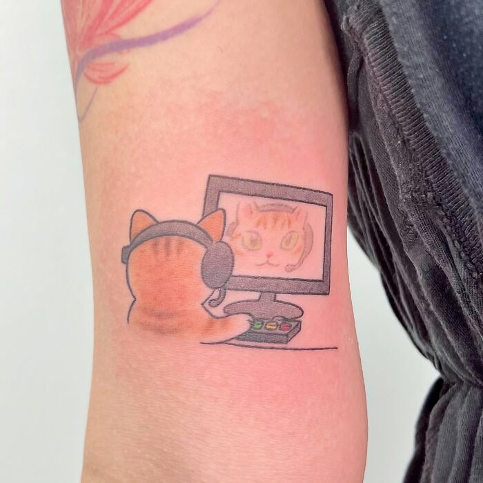 Tattoo of an adorable cat wearing headphones playing on a computer, showcasing Korean artist Buoy’s animal tattoo style.