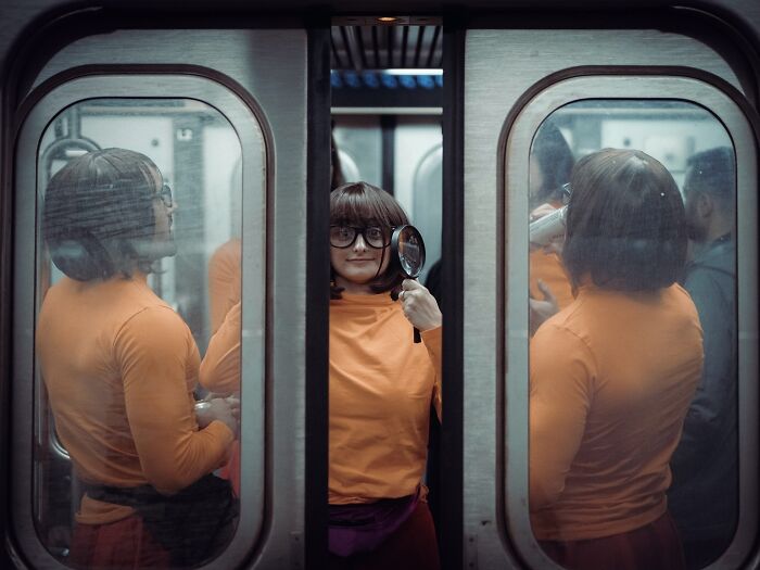 Woman in an orange top holding a magnifying glass inside a crowded subway train, a striking street photo with a cinematic feel.