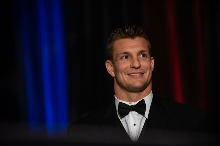 Man in a black tuxedo and bow tie smiling against a dark background representing celebrity encounters with worst experiences.